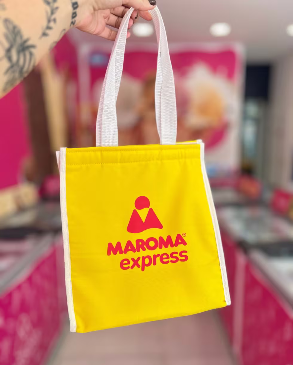 Sacola térmica amarela da Maroma Express segurada em frente à loja